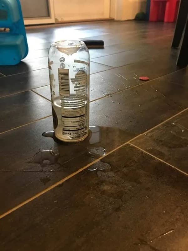 Upside down plastic bottle standing in a puddle of spilled liquid on a tile floor