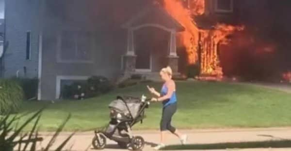 Woman pushing a stroller along a sidewalk as a house burns in the background