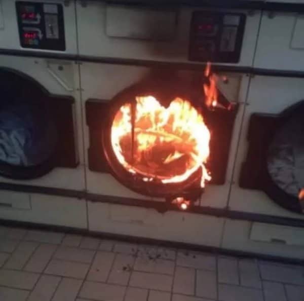 Laundromat dryer engulfed in flames with fire pouring out of the round door