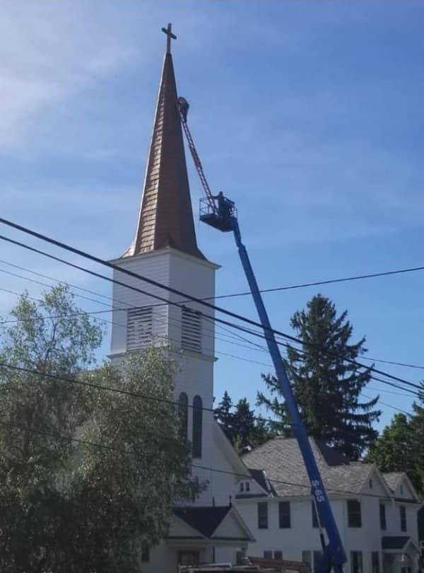 Worker on a tall lift reaching the very top of a church steeple near power lines