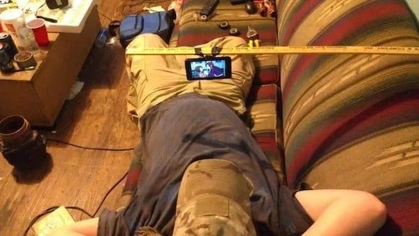 Man lying on a couch watching a phone mounted to a yardstick laid across the cushions.