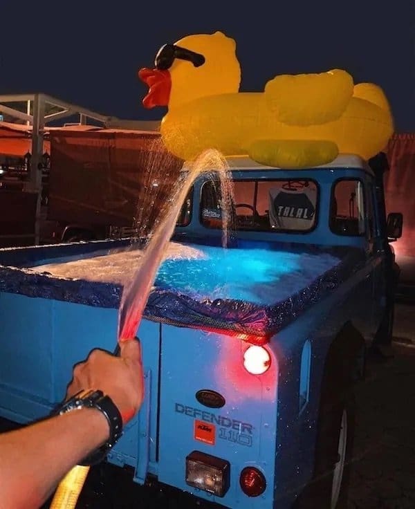 Pickup truck bed lined with a tarp and filled as a hot tub, inflatable duck on the roof.