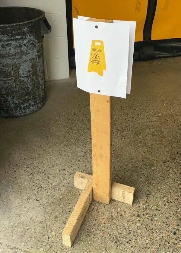Homemade wet floor sign made from a printed picture stapled to a wooden stand.