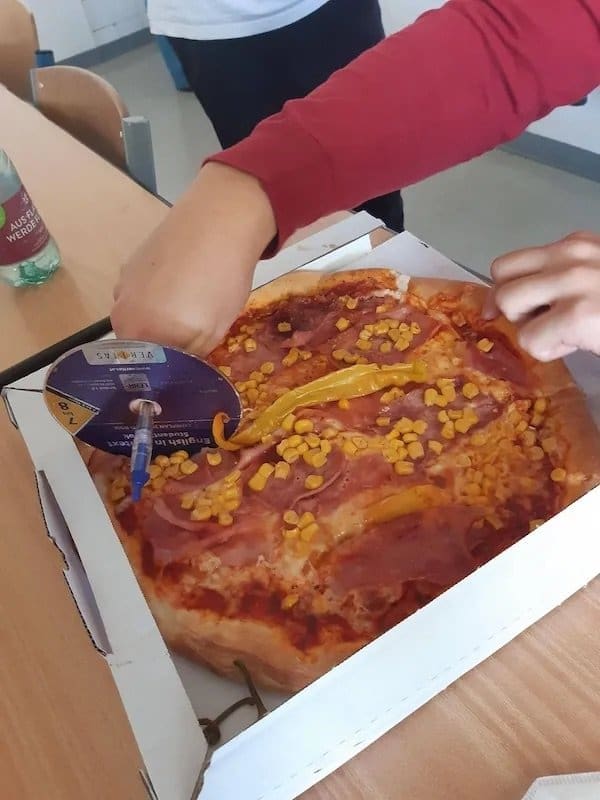 Pizza being sliced with a CD and a pen used as a makeshift pizza cutter.