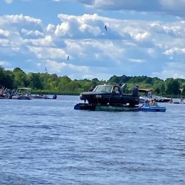 Pickup truck floating on a platform of barrels in the middle of a busy lake.