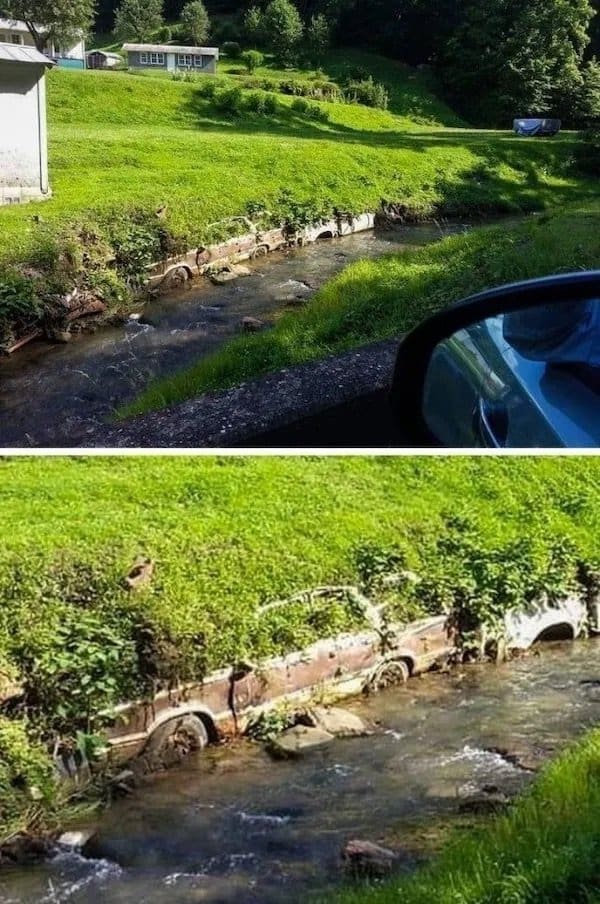 Old car buried in a creek bank as a retaining wall, now overgrown with grass.