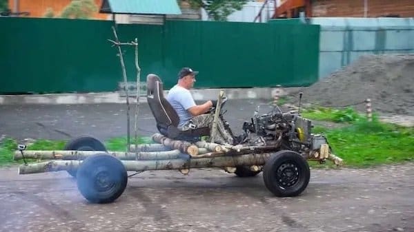 Man driving a homemade vehicle built from birch logs, an engine, and an old seat.
