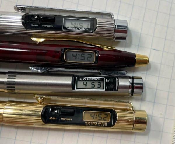 Four vintage metallic writing pens featuring integrated digital LCD clocks built directly into the barrels as retro tech.