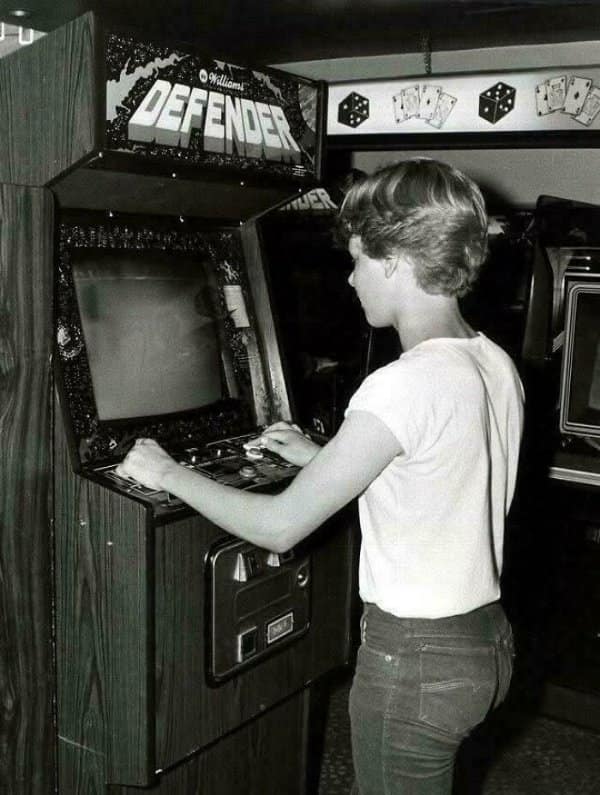 Black-and-white photograph of a kid intensely playing a classic Williams Defender arcade cabinet in a retro tech setting.