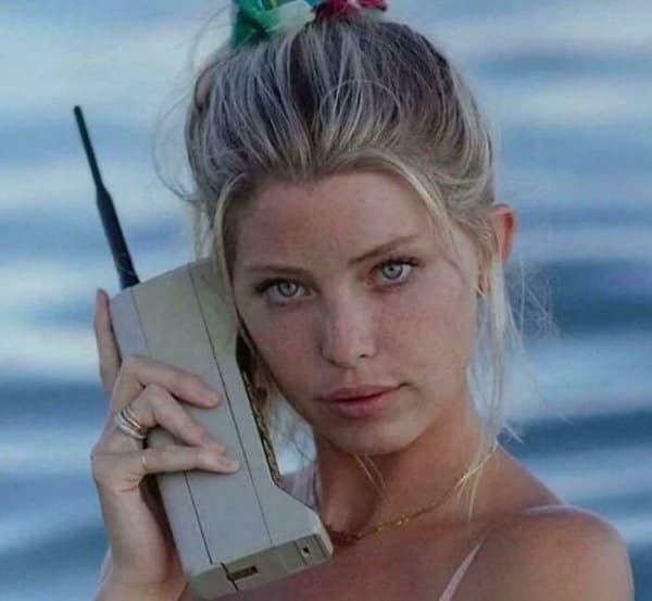 Close-up portrait of a woman holding a giant 1980s brick cell phone with a thick antenna as retro tech.