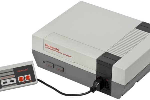 Studio shot of a classic gray Nintendo Entertainment System (NES) console connected to a two-button controller as retro tech.
