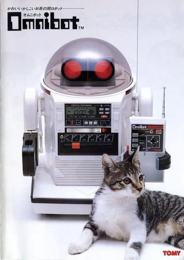 Vintage Tomy Omnibot toy robot with a built-in cassette player deck sitting next to a domestic cat in a retro tech product photo.