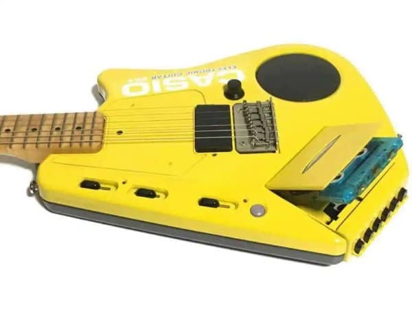 Bright yellow Casio EG-5 cassette guitar featuring an integrated tape deck and onboard speaker in a retro tech showcase.