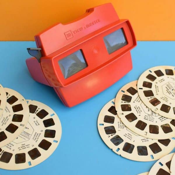 Classic red 3D View-Master toy viewer displayed alongside several circular cardboard image reel discs in a retro tech setup.
