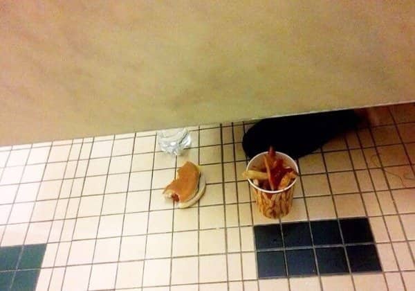 Hot dog and fries sitting on a bathroom floor below a stall with a foot visible