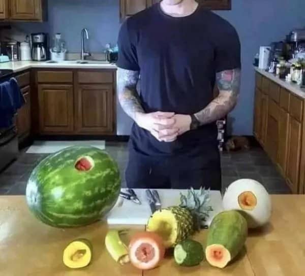 Man standing behind a kitchen table of fruits and vegetables with holes cut in each one
