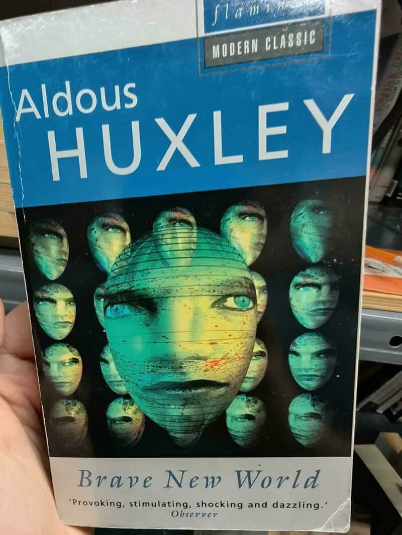 Brave New World paperback with a cover of eerie floating green masks and one central face.