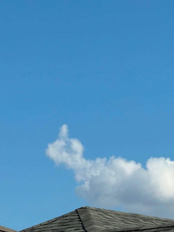 Fluffy white cloud shaped like a rude hand gesture floating above a neighbor's rooftop.