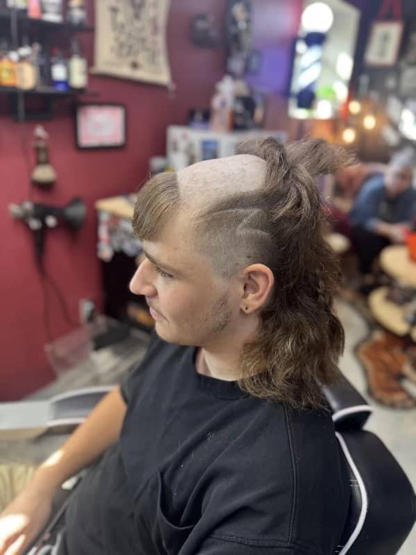 Young man in a barbershop with a shaved strip across his head and a long mullet
