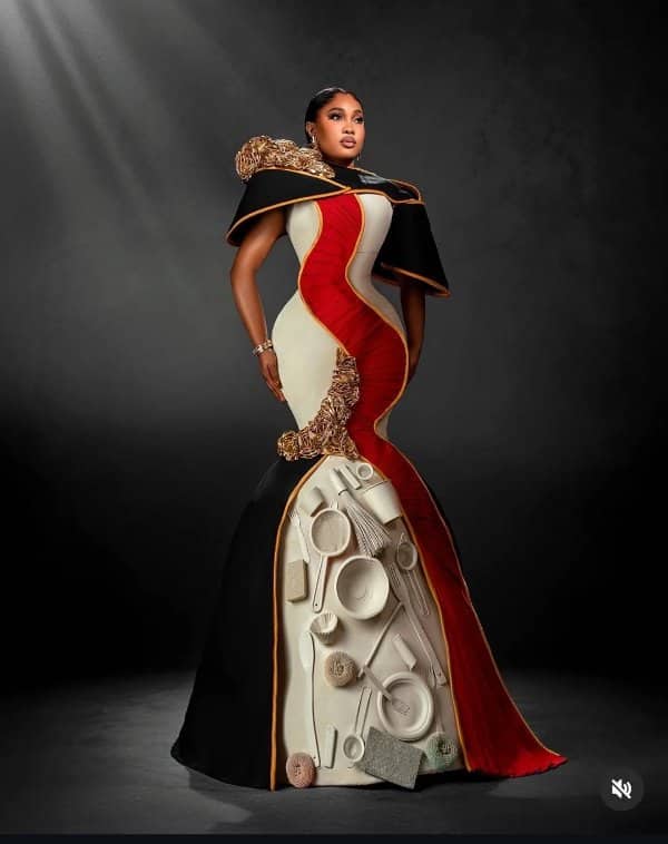 Woman posing in a sculpted red, cream, and black gown decorated with kitchen utensils