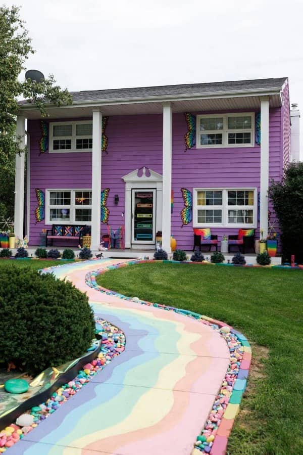 Purple two story house with butterfly decorations and a rainbow painted walkway out front