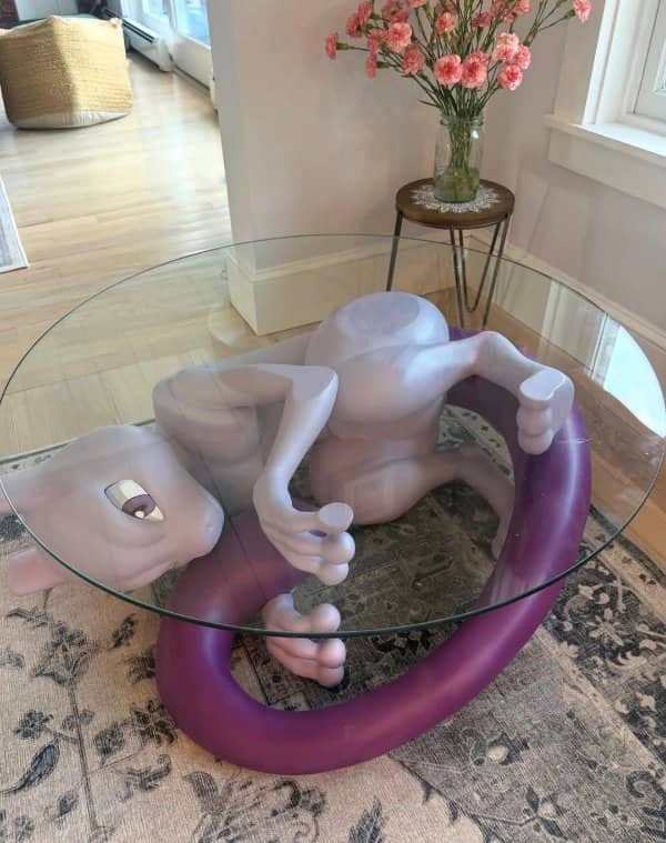 Glass coffee table with a large Mewtwo sculpture curled beneath it on a patterned rug