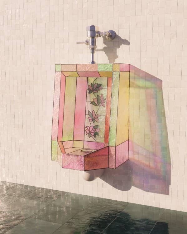 Wall mounted urinal covered in pink and green stained glass with a floral center panel