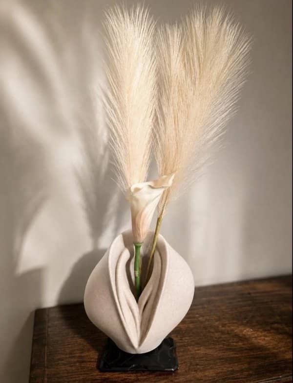 Cream ceramic vase with a curved, folded shape holding pampas grass and a calla lily