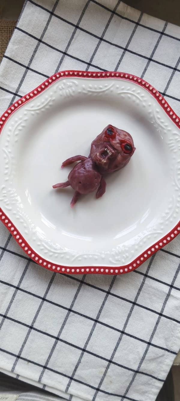 Purple sculpted food shaped like a screaming creature with red eyes on a white plate