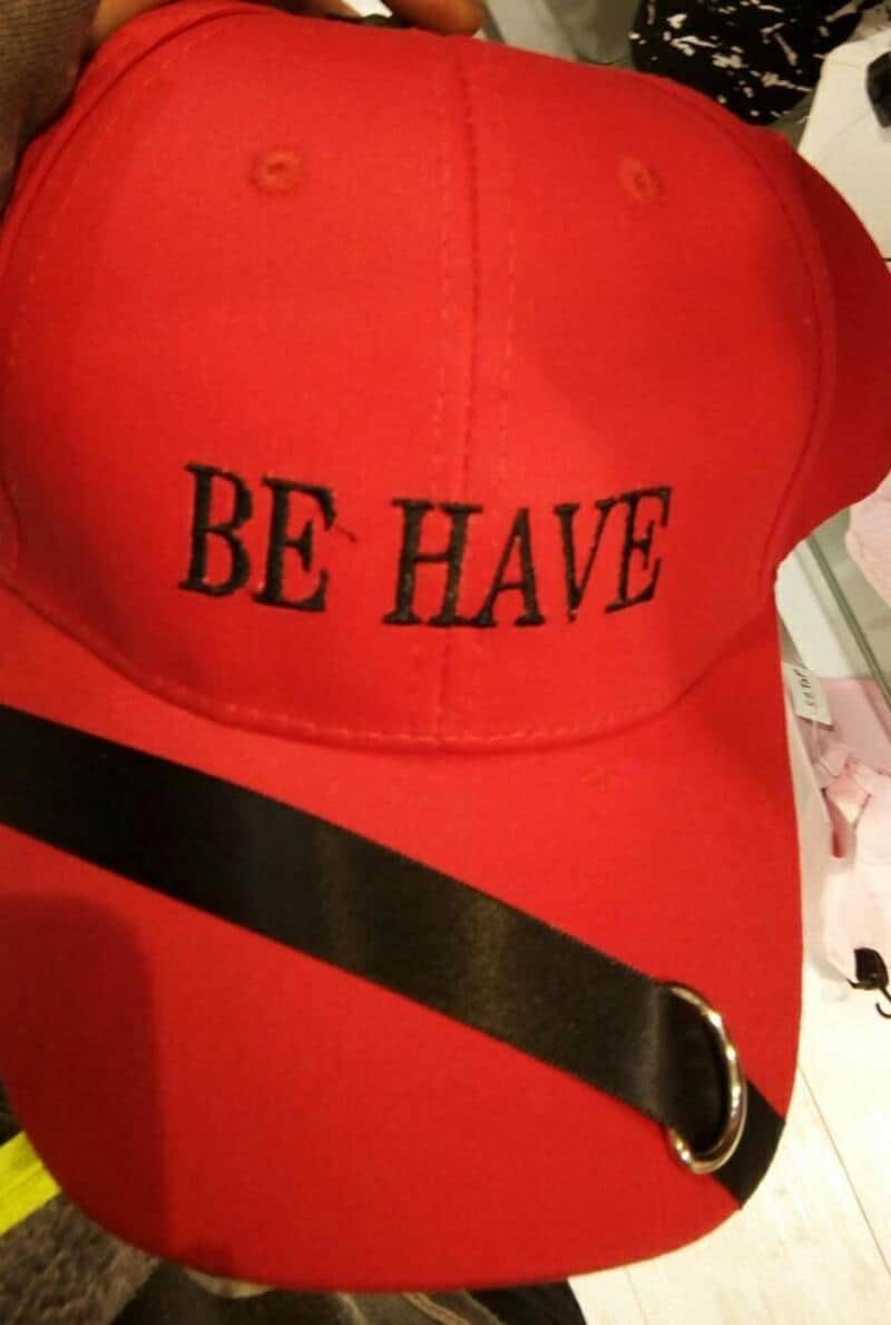 Red baseball cap embroidered with BE HAVE in widely spaced black letters