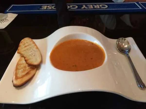 Bowl of tomato soup served on a wavy white novelty plate with toasted bread