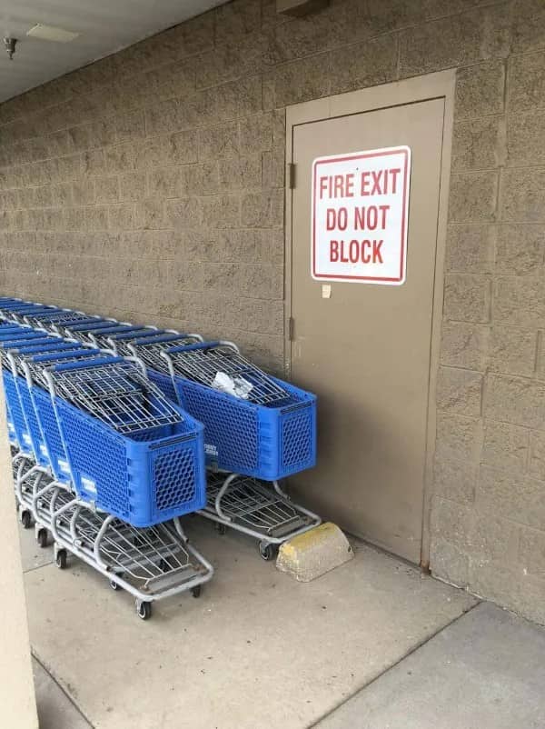 Row of blue shopping carts parked against a door labeled Fire Exit Do Not Block