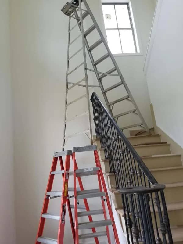 Tall extension ladder balanced on a staircase with an orange stepladder in front