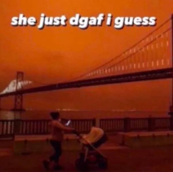 Woman pushing a stroller while scrolling her phone under an orange wildfire smoke sky