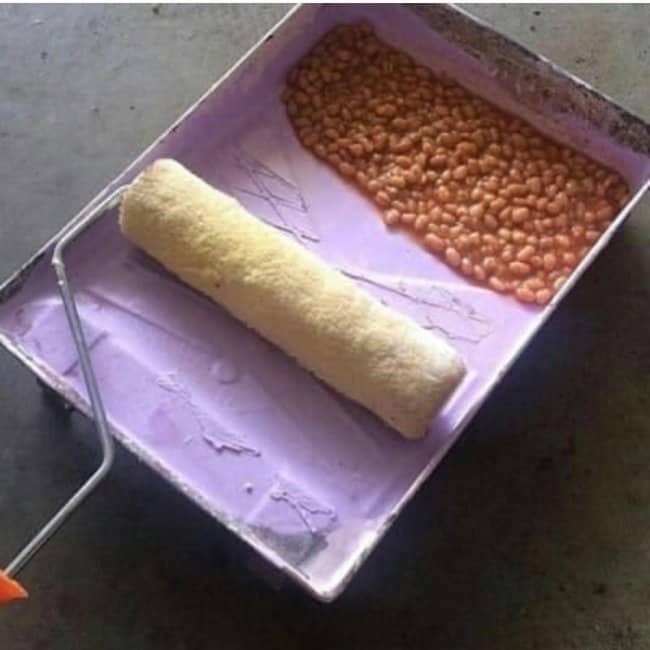 Lavender paint tray with a roller and a pile of baked beans where the paint should be.