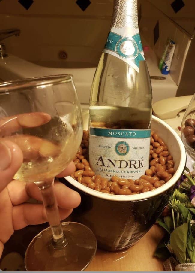 Bottle of André Moscato chilling in a bucket of baked beans instead of ice, glass raised.