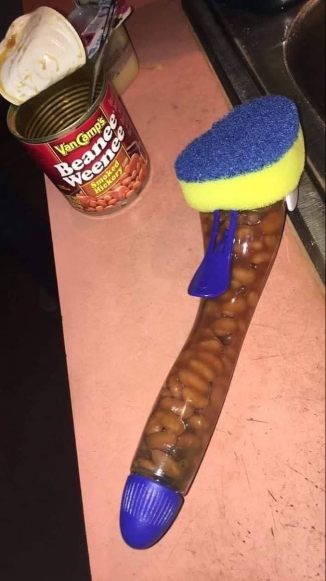 Dish wand brush filled with baked beans beside an open can of Beanee Weenee on a counter.