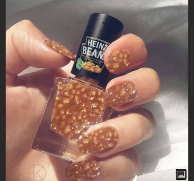 Hand with fingernails coated in baked beans, holding a Heinz Beanz nail polish bottle.