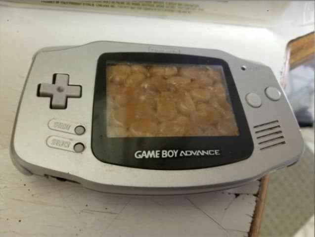 Silver Game Boy Advance with the screen area filled with baked beans behind the glass.