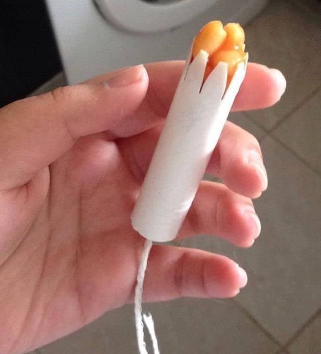 Hand holding a tampon applicator with baked beans poking out the top.