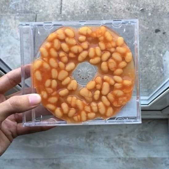Hand holding a clear CD jewel case with baked beans arranged in a ring like a disc.
