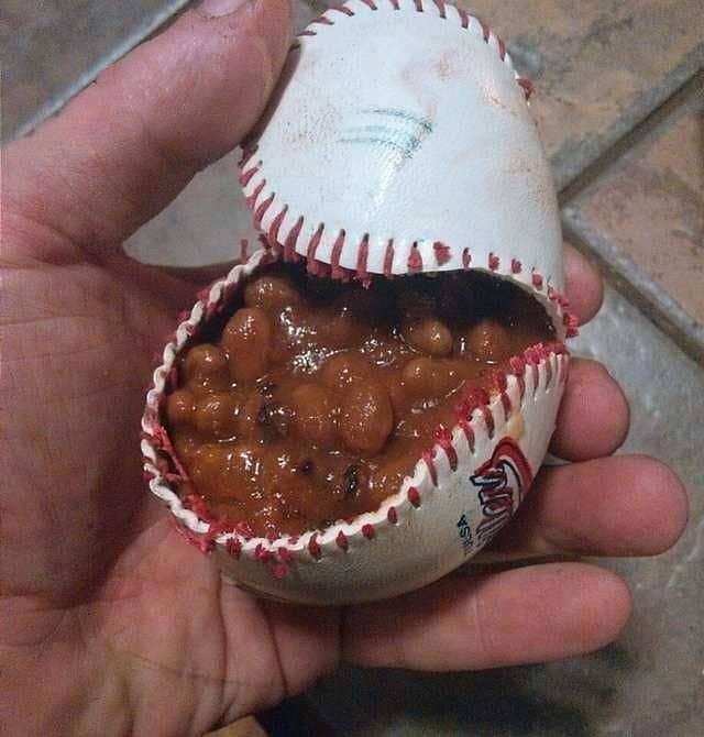 Baseball split open at the seams like a pouch, filled with baked beans and held in a hand.