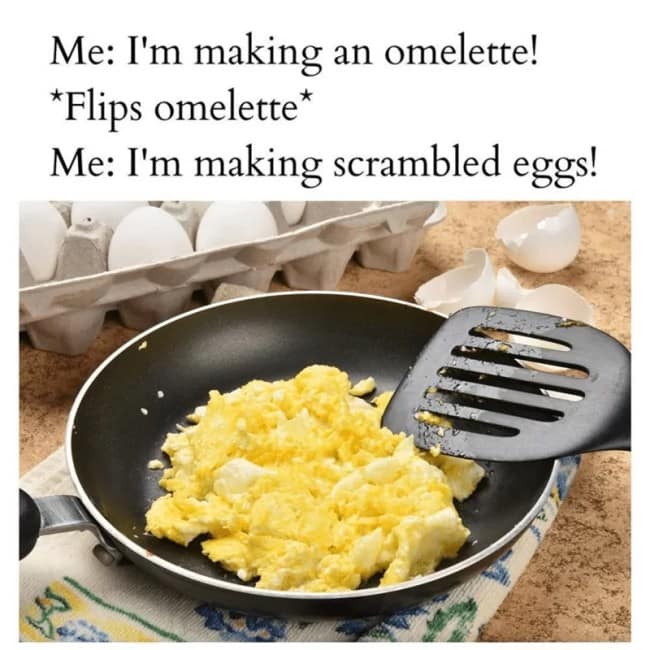 Pan of scrambled eggs after a failed omelette flip, beside an egg carton.