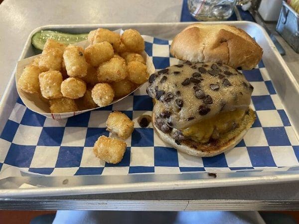 Cheeseburger topped with melted cheese and what look like chocolate chips, with tater tots.