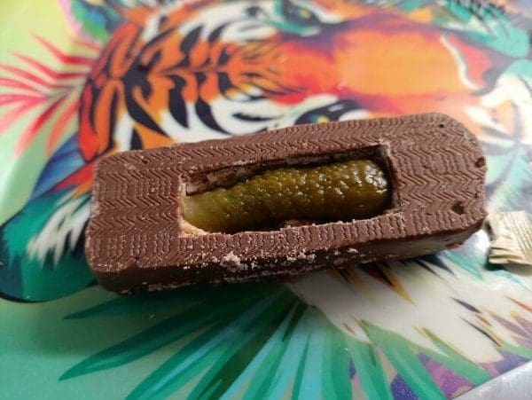 Weird food snack: a chocolate bar bitten open to show a whole pickle inside.