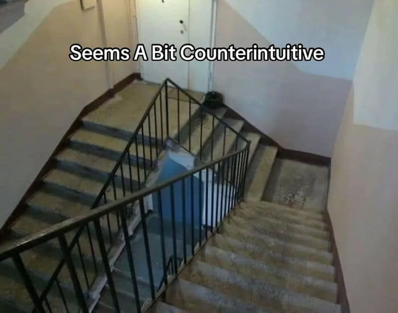 Apartment stairwell where two flights collide awkwardly, with a railing cutting right across the steps.