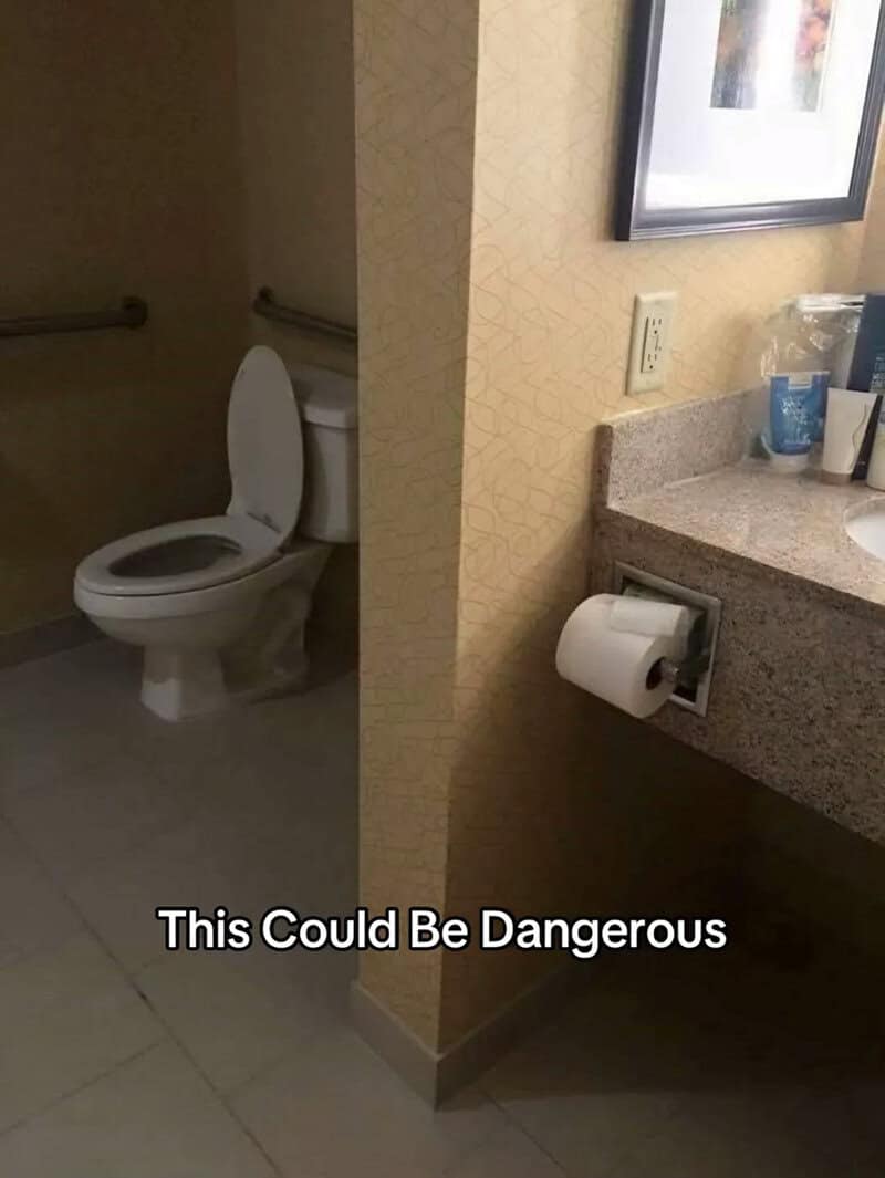 Hotel bathroom with the toilet paper holder installed around a wall corner from the toilet.