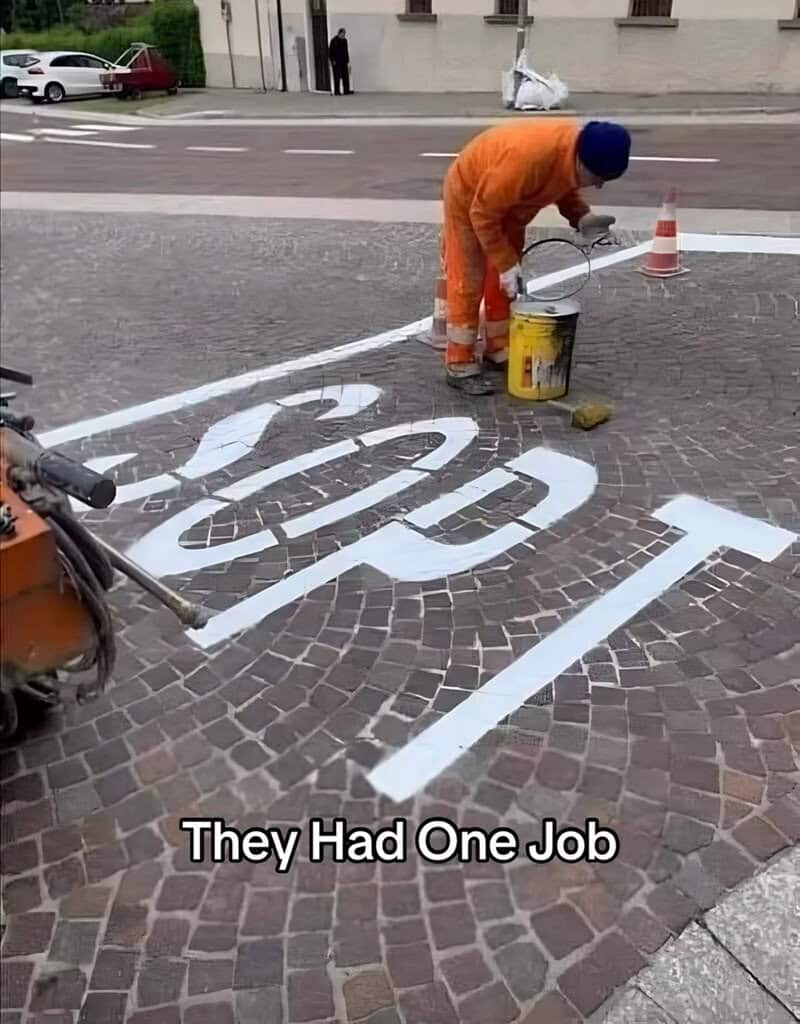 Road worker painting large white letters onto a cobblestone street, with the word clearly painted wrong.