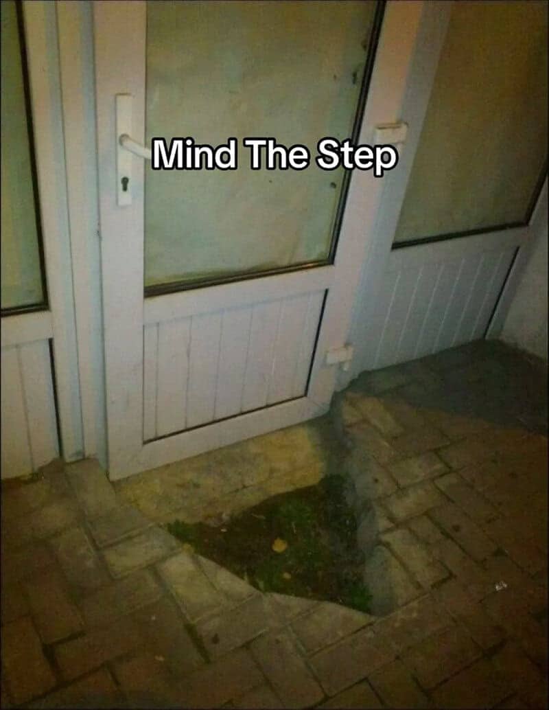 Glass door that opens directly onto a deep sunken hole in the paved walkway outside.