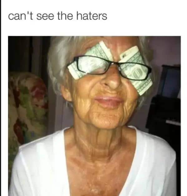 Elderly woman wearing glasses with dollar bills tucked behind the lenses, captioned can't see the haters.
